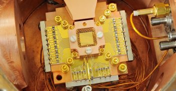 An apparatus to coax two beryllium ions (electrically charged atoms) into swapping the smallest measurable units of energy back and forth, a technique that may simplify information processing in a quantum computer. The ions are trapped about 40 micrometers apart above the square gold chip in the center. The chip is surrounded by a copper enclosure and gold wire mesh to prevent buildup of static charge. Source: Y. Colombe/NIST https://bit.ly/2XMIwfU