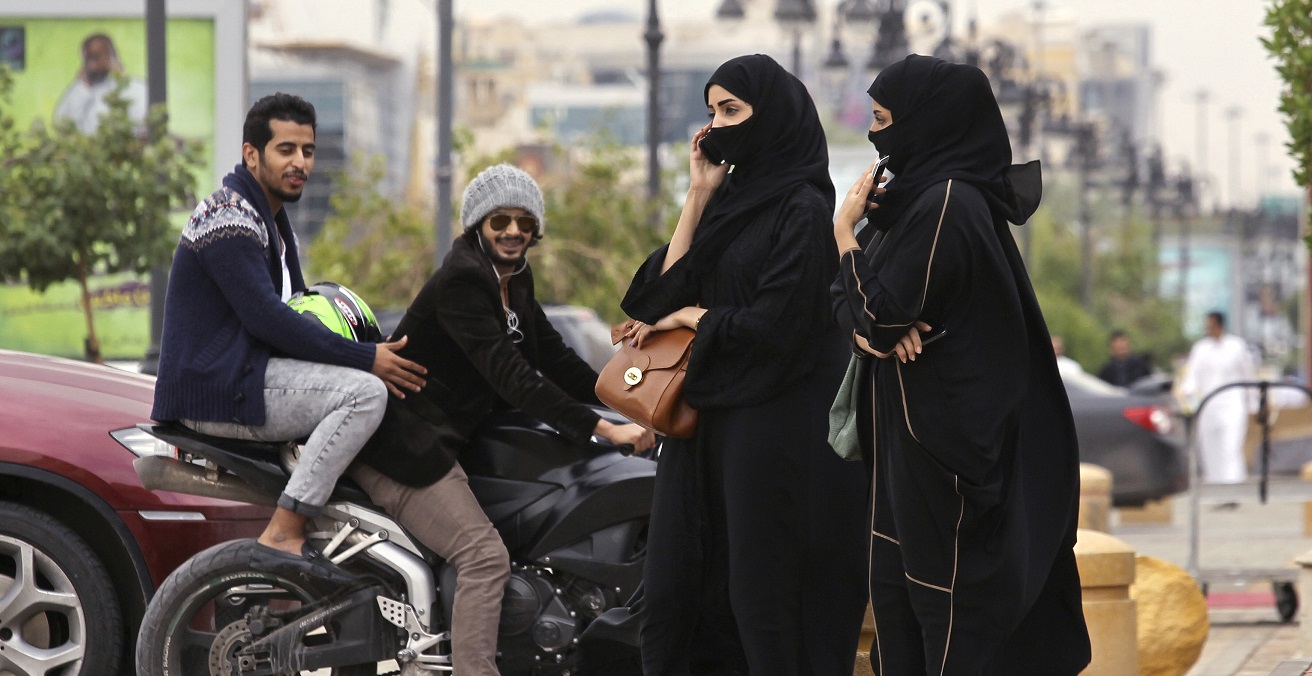 A woman speaks on the phone as men ride a motorcycle on a cloudy day in Riyadh November 17, 2013. Source: Jess Pink https://bit.ly/3qAuER0